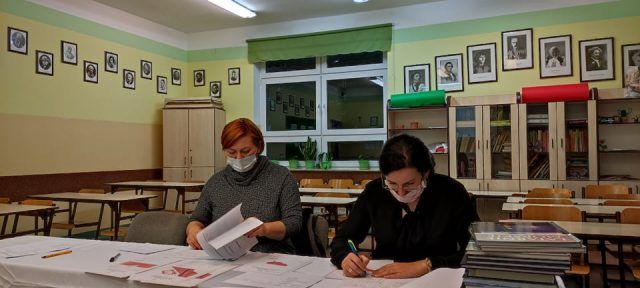 W szkolnej klasie Anna Górka i Izabela Miętus siedząc przy stole oceniają prace konkursowe.