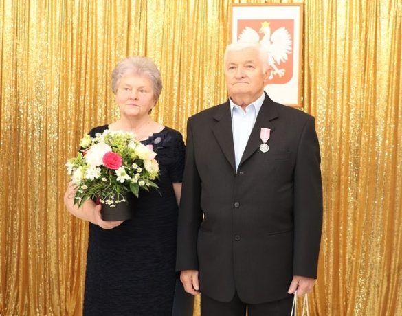 Para odznaczona medalem, trzymająca w ręku kwiaty, list gratulacyjny oraz upominek
